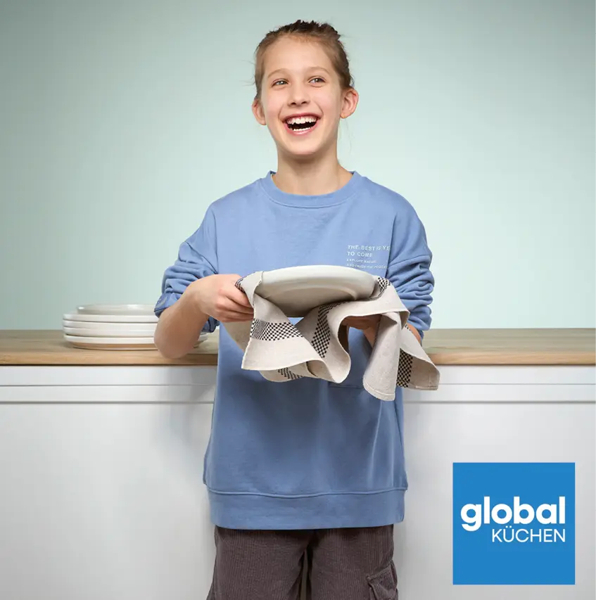 Person im blauen Sweatshirt trocknet weissen Teller mit Geschirrtuch vor Tellerstapel, unten rechts blaues Logo mit Schriftzug global Küchen.